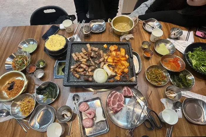 테이블에 푸짐하게 차려진 다양한 밑반찬과 메인 메뉴를 기다리는 모습