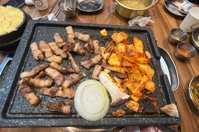 불판 위에서 노릇하게 익어가는 삼겹살과 콩나물, 김치