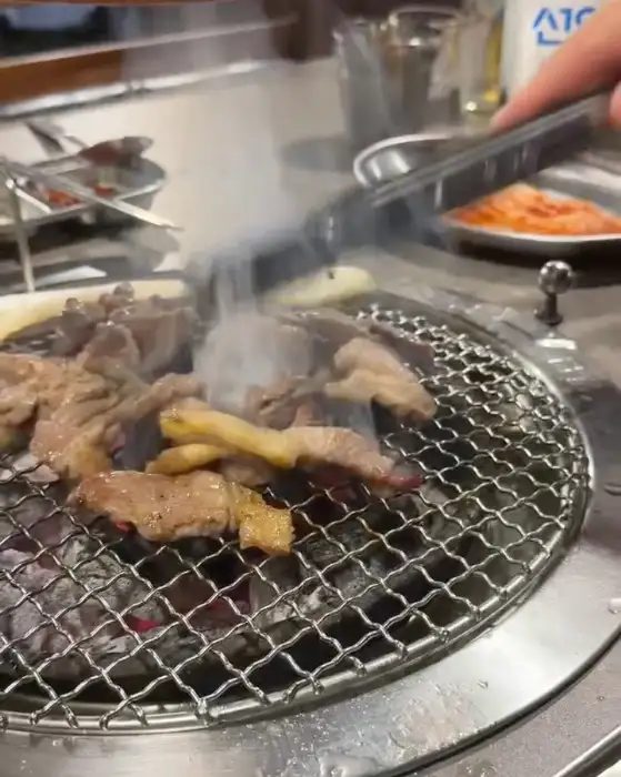 집게로 집어 올린 돼지고기에서 맛있는 연기가 피어오르고 있는 모습