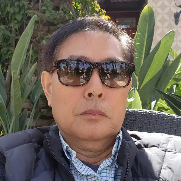 선글라스를 낀 중년 남성의 클로즈업 사진. 배경에는 녹색 식물들이 보인다.
