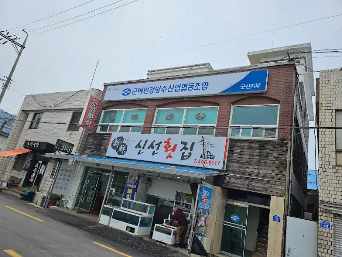 건물 정면에 '신선 횟집'이라는 커다란 현수막이 걸려 있고, 그 아래로 '군산 횟집'이라는 글씨와 전화번호가 보인다.