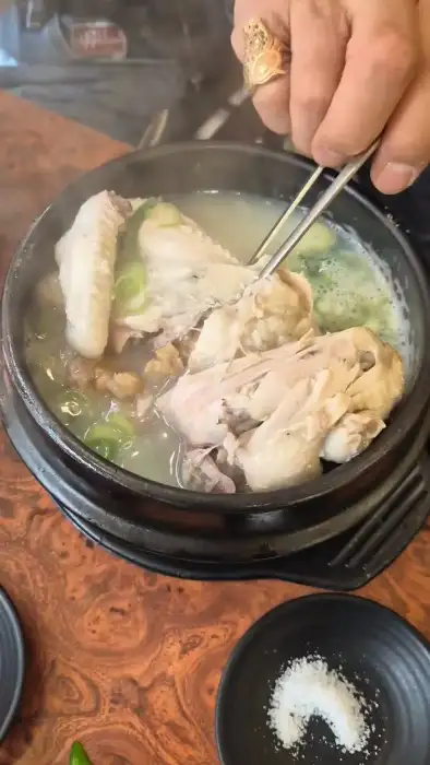 젓가락으로 삼계탕 닭고기를 들어 올리는 모습