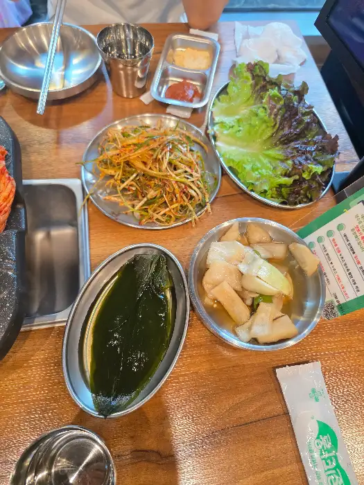 상추, 깻잎, 콩나물 무침, 묵사발 등이 식탁 위에 보기 좋게 차려져 있습니다.