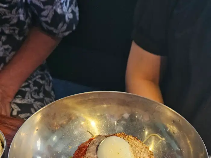 금속 그릇에 담긴 비빔냉면의 모습. 고명으로 계란과 채소들이 올려져 있다.