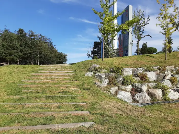 푸른 잔디밭과 돌로 쌓은 경사면에 나무가 서 있고, 계단이 보인다.