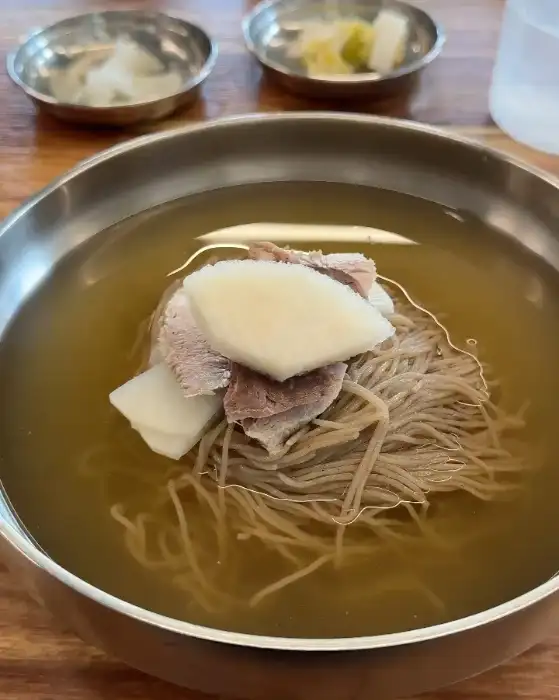 평양냉면 위에 얇게 썬 고기와 하얀 무 조각이 올라간 모습
