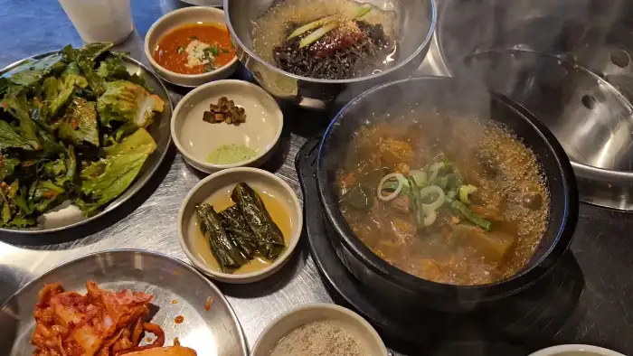 푸짐하게 차려진 테이블 모습, 가운데 김치와 쌈 채소가 놓여있고, 그 뒤로 해장국과 냉면이 보인다.