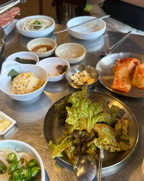 테이블에 차려진 다양한 밑반찬들. 쌈 채소, 김치, 젓갈류, 동치미 등이 보인다.