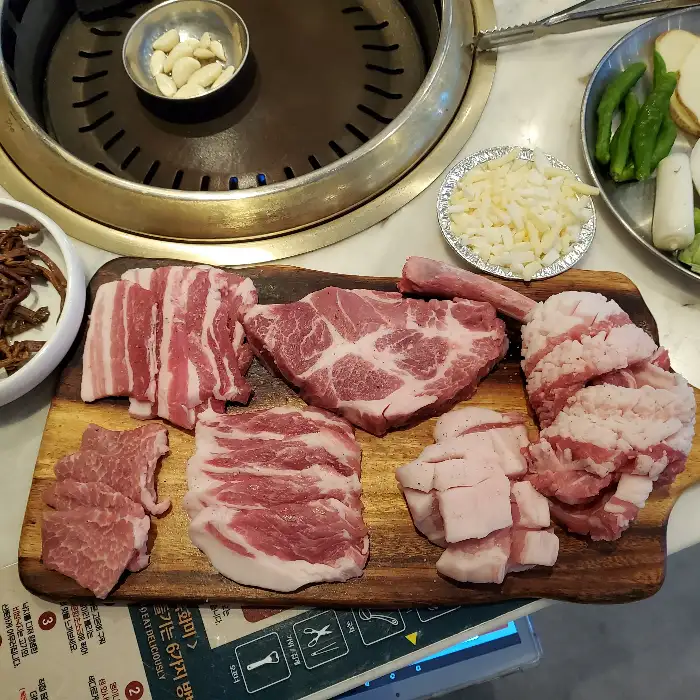 신선한 삼겹살과 목살이 먹기 좋게 썰어져 나무 도마 위에 놓여 있습니다.