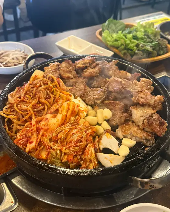 잘 익어가는 삼겹살 주변으로 김치와 마늘, 버섯이 함께 올라가 있습니다.