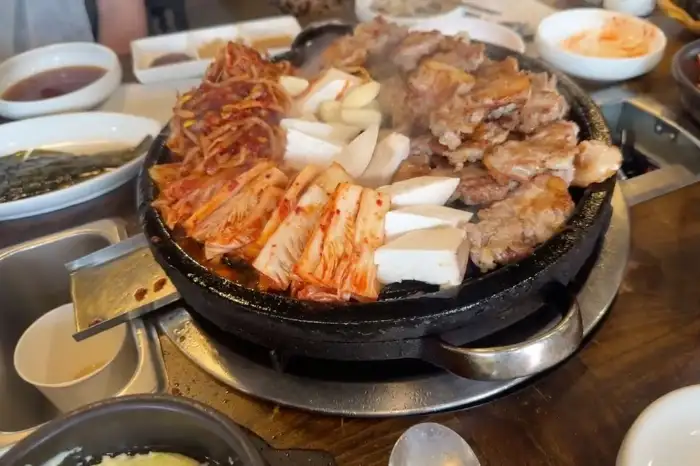 돌판에 푸짐하게 담긴 삼겹살과 김치, 콩나물의 모습