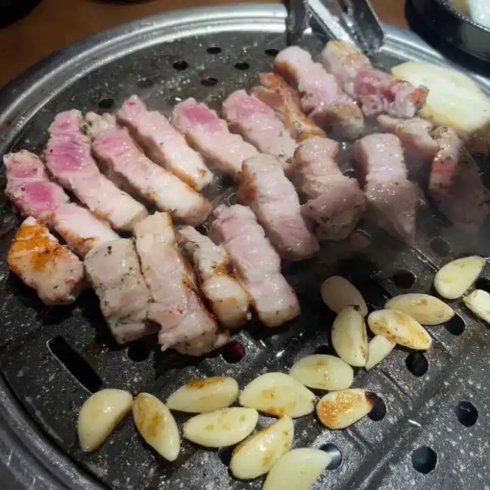 불판 위에서 맛있게 구워지고 있는 삼겹살과 꼬들살, 그리고 마늘