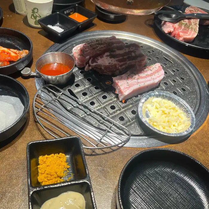 테이블에 차려진 돼지고기, 쌈 채소, 김치, 소스 등 다양한 반찬들