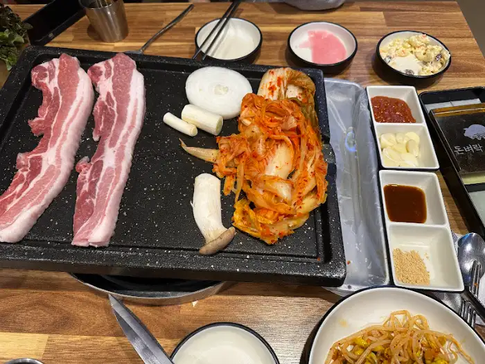 불판 위 삼겹살과 김치, 곁들임 반찬