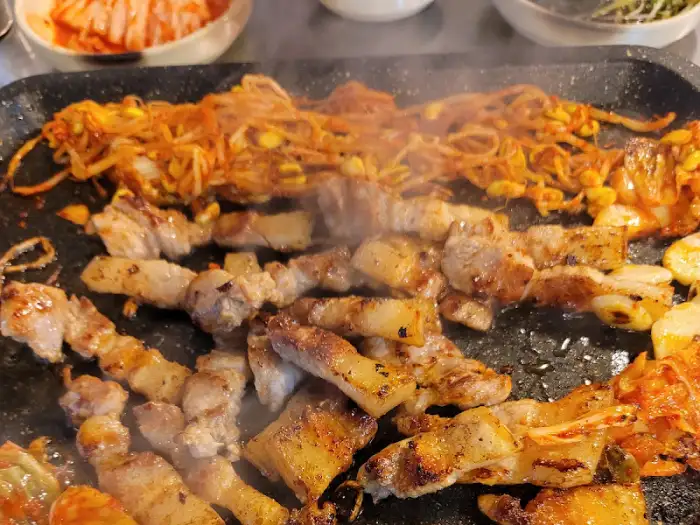 불판 위에서 익고 있는 삼겹살과 곁들임 음식들