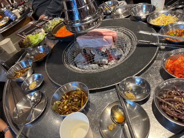 식탁 위에 차려진 다양한 밑반찬과 구워지는 고기