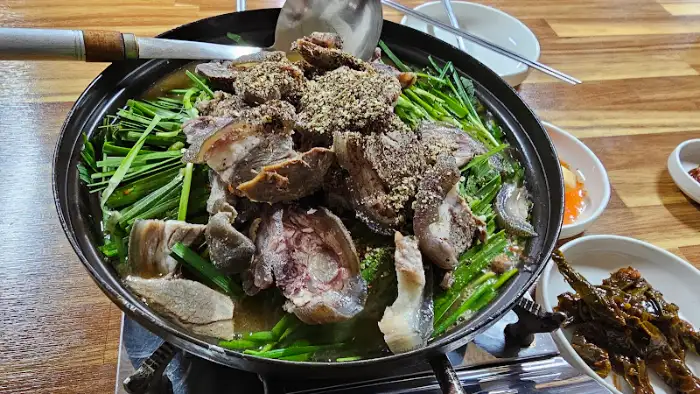 흑염소 전골 냄비의 클로즈업 샷. 흑염소 고기의 질감이 생생하게 보이고, 국물에 녹아든 채소들의 색감이 식욕을 자극한다.