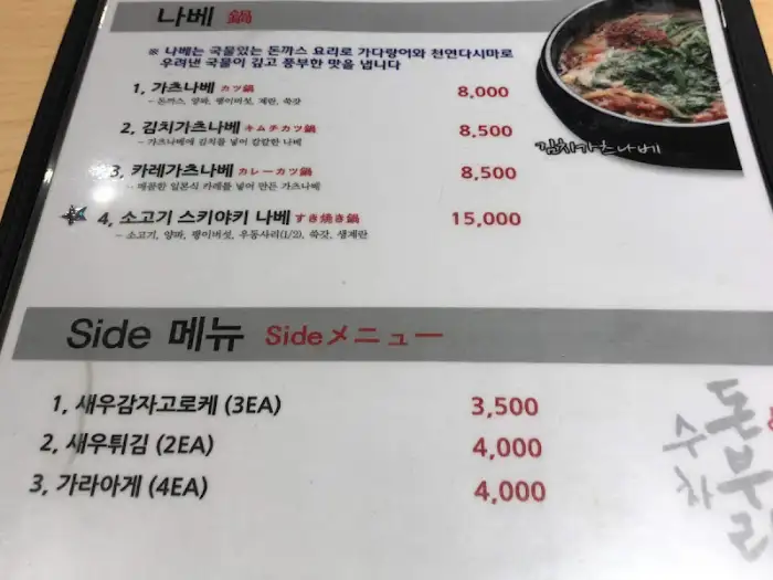 메뉴판 일부 모습. '나베'와 'Side 메뉴' 섹션의 가격 정보가 보입니다. '가츠나베' 8,000원, '김치나베' 8,500원, '카레나베' 8,500원, '소고기 스키야키 나베' 15,000원 등 다양한 메뉴가 나열되어 있습니다.