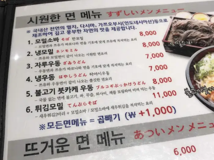 메뉴판 일부 모습. '시원한 면 메뉴' 섹션의 가격 정보가 보입니다. '모밀소바' 8,000원, '냉모밀' 7,000원, '자루우동' 7,000원, '냉우동' 8,000원, '불고기 카레 우동' 11,000원, '튀김모밀' 8,000원 등이 나열되어 있습니다.