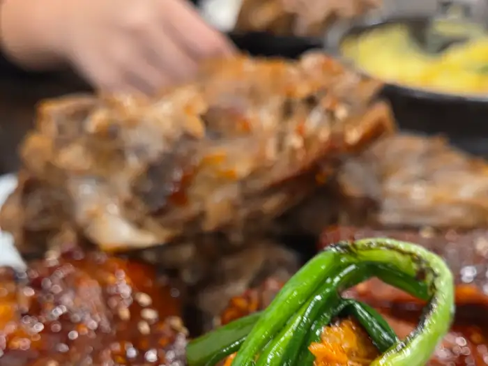 빨간 양념 뼈구이 위에 싱싱한 파채가 올려져 있고, 뒤쪽에는 다른 뼈구이와 계란찜이 보입니다.