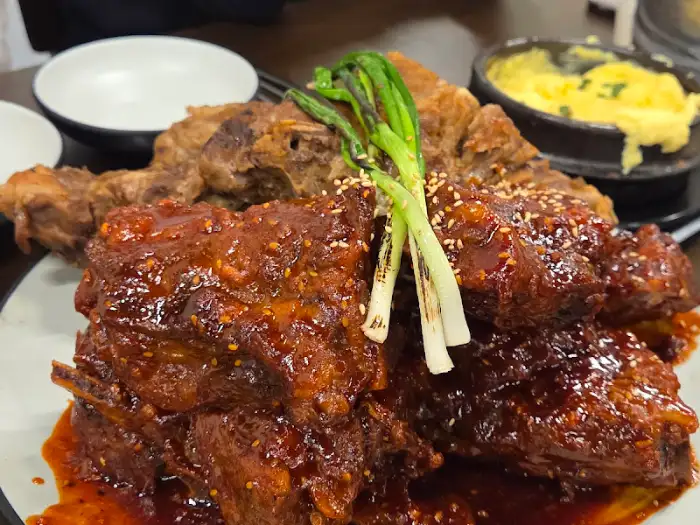 반반 뼈구이 한 접시에 소금구이와 양념구이가 나란히 담겨 있고, 녹색 파가 장식처럼 얹어져 있습니다. 뒤쪽에는 계란찜이 놓여 있습니다.