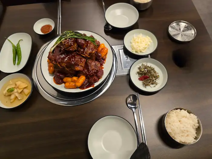 테이블 위에 뼈구이, 밥, 계란찜, 반찬 등이 차려져 있는 모습. 정갈하게 세팅된 상차림이 인상적입니다.