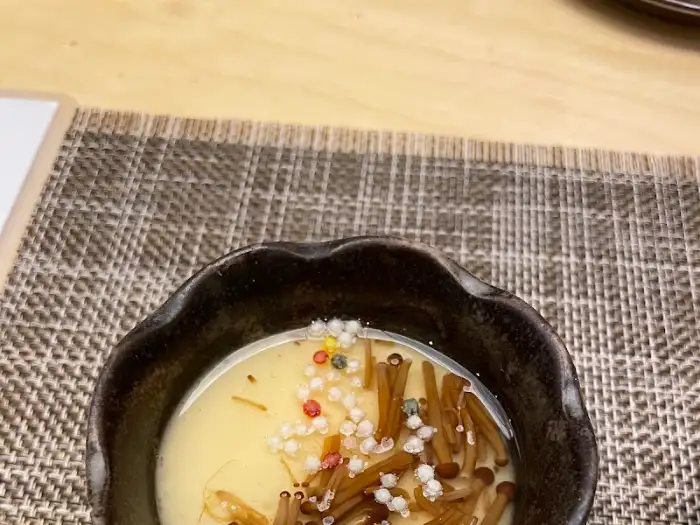 따뜻하고 부드러운 계란찜 위에 버섯과 작은 알갱이들이 올라간 요리