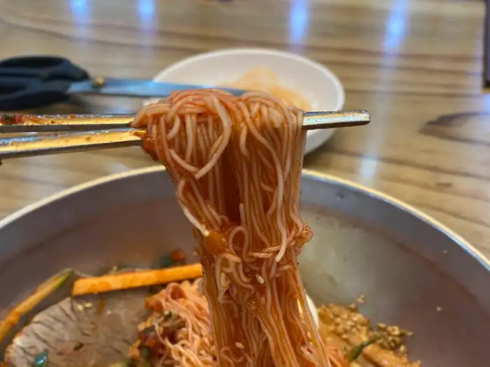 집게로 비빔냉면 면발을 집어 올리는 모습