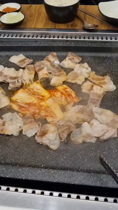 불판에 김치, 콩나물, 버섯 등 다양한 채소와 함께 구워지고 있는 대패삼겹살