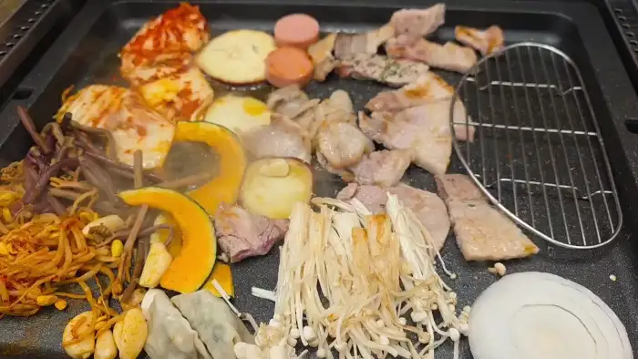 불판 위에 김치, 호박, 버섯, 콩나물, 떡 등 다양한 재료와 함께 구워지고 있는 고기