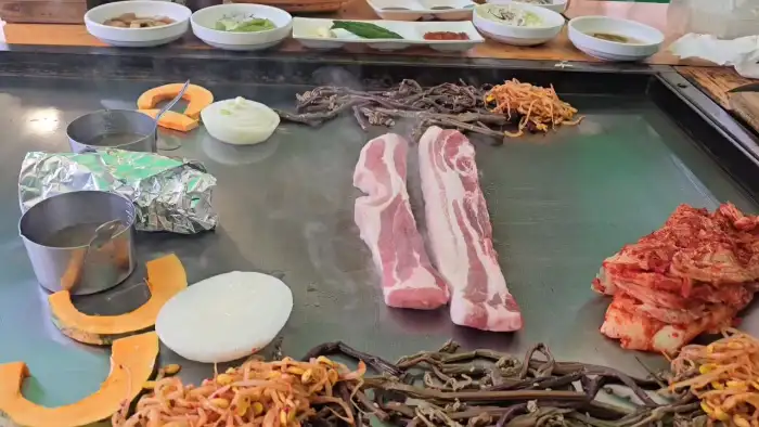 넓은 철판 위에 올려진 삼겹살과 반찬들
