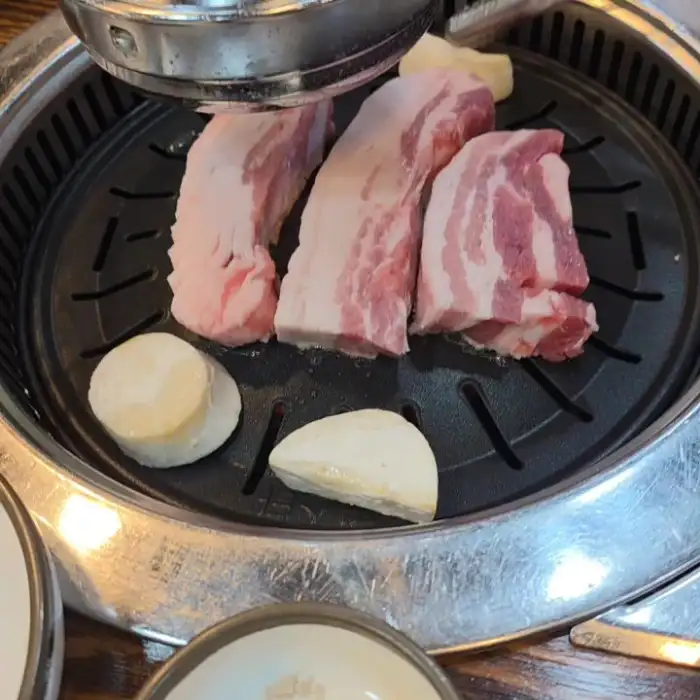 두툼한 삼겹살 덩어리가 불판 위에 올라가 있는 모습