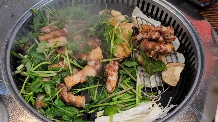 삼겹살과 함께 여러 채소들이 불판 위에서 익어가고 있는 모습
