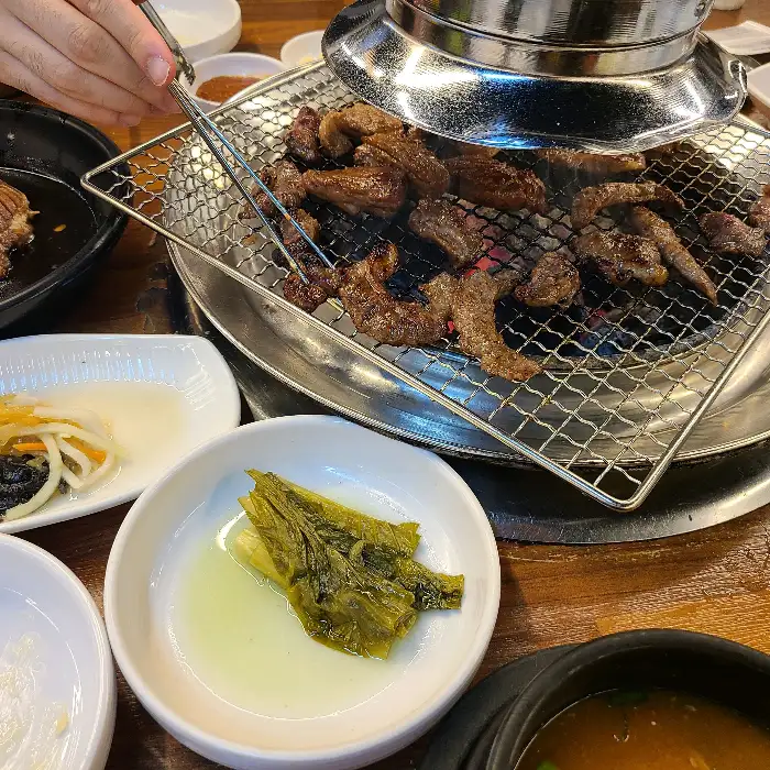젓가락으로 돼지갈비를 집어 숯불 위에서 익히는 모습