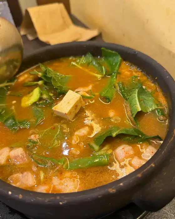 김치찌개가 뚝배기에 담겨 있고, 녹색 채소가 듬뿍 올라가 있다.