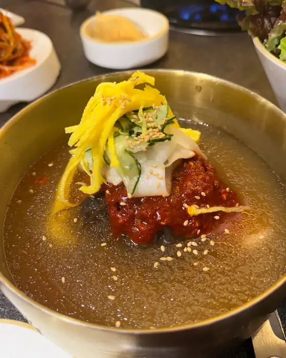 놋그릇에 담긴 비빔냉면으로, 고명으로 채 썬 오이, 계란 지단, 그리고 붉은 양념이 올라가 있다.