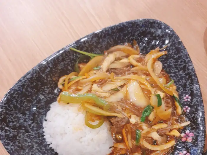 밥 위에 볶음 요리가 올라간 모습. 당면, 채소, 고기가 어우러져 있다.