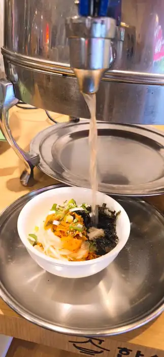 잔치국수 그릇에 국물이 부어지고 있는 모습.