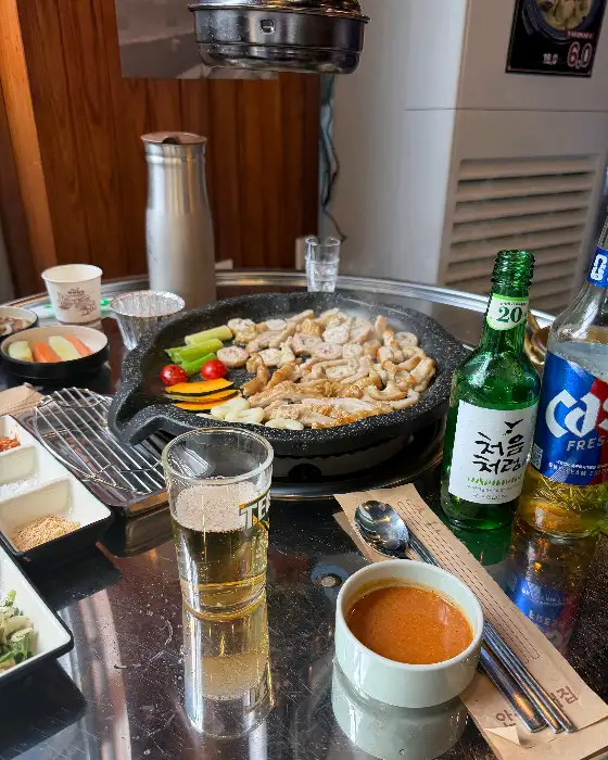 테이블 위에 맥주잔, 소주잔, 간장 종지, 쌈장 종지, 양념된 막창이 올려진 돌판이 보입니다.