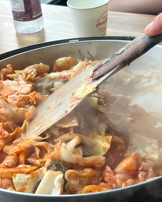 지글지글 끓는 닭갈비 팬의 모습, 김이 모락모락 피어오르며 맛있는 냄새를 풍긴다.