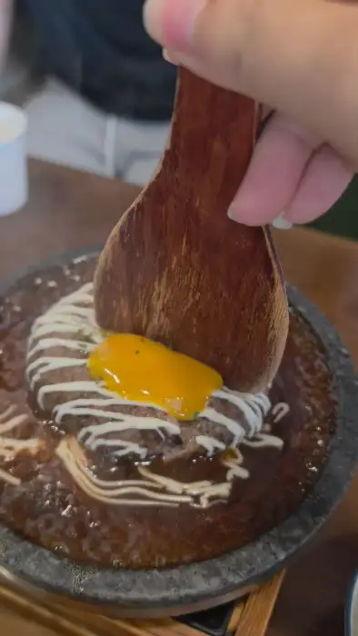 뜨거운 돌판에 담겨 나온 함박스테이크에 계란 노른자를 곁들이는 모습