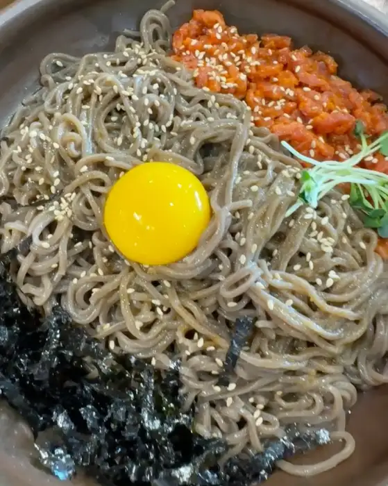 메밀면 위에 신선한 육회가 올라가고 계란 노른자가 얹어진 비빔 막국수