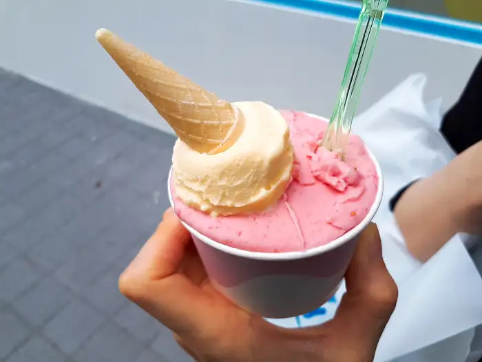 컵에 담긴 핑크색 딸기맛 젤라또와 그 위에 올려진 노란색 아이스크림, 그리고 작은 콘
