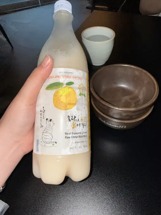 새콤달콤한 막걸리 라벨이 보이는 병과 컵, 그릇