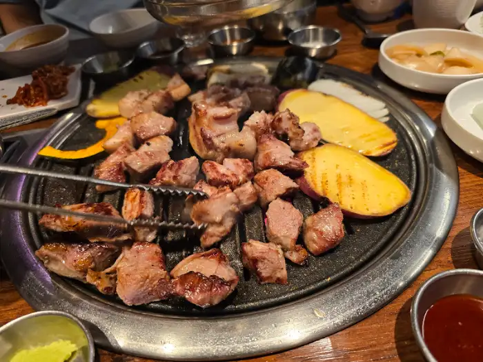 불판 위에서 맛있게 구워지고 있는 삼겹살과 목살, 곁들임 채소