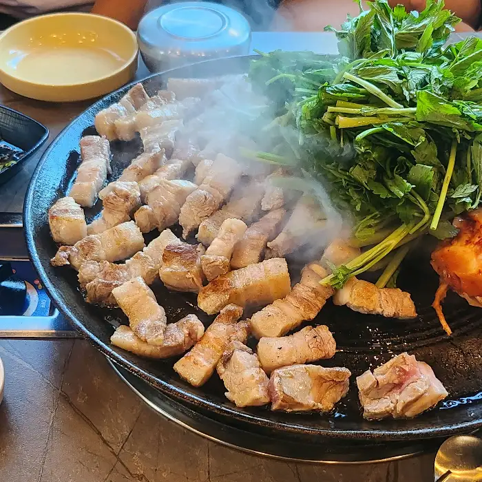 솥뚜껑 위에서 구워지고 있는 삼겹살과 미나리, 김치