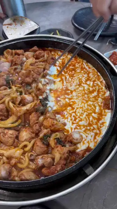 철판의 반은 닭갈비와 사리가 조리되고 있고, 나머지 반은 녹아내리는 치즈로 덮여 있습니다.