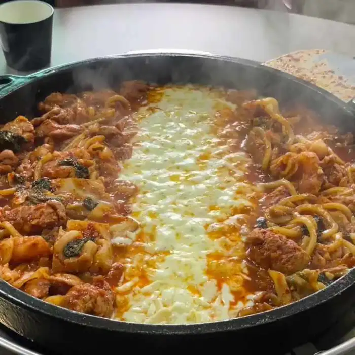 치즈가 녹아내리면서 닭갈비와 함께 섞이고 있습니다. 닭갈비에는 떡, 양배추 등의 채소가 함께 들어있습니다.