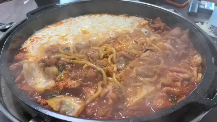 철판에 닭갈비와 치즈, 우동 사리가 푸짐하게 담겨 있습니다.