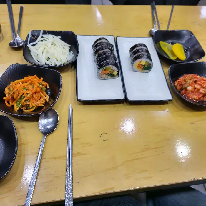 테이블에 김밥, 곁들임 찬, 젓가락, 숟가락 등이 정갈하게 세팅되어 있습니다.